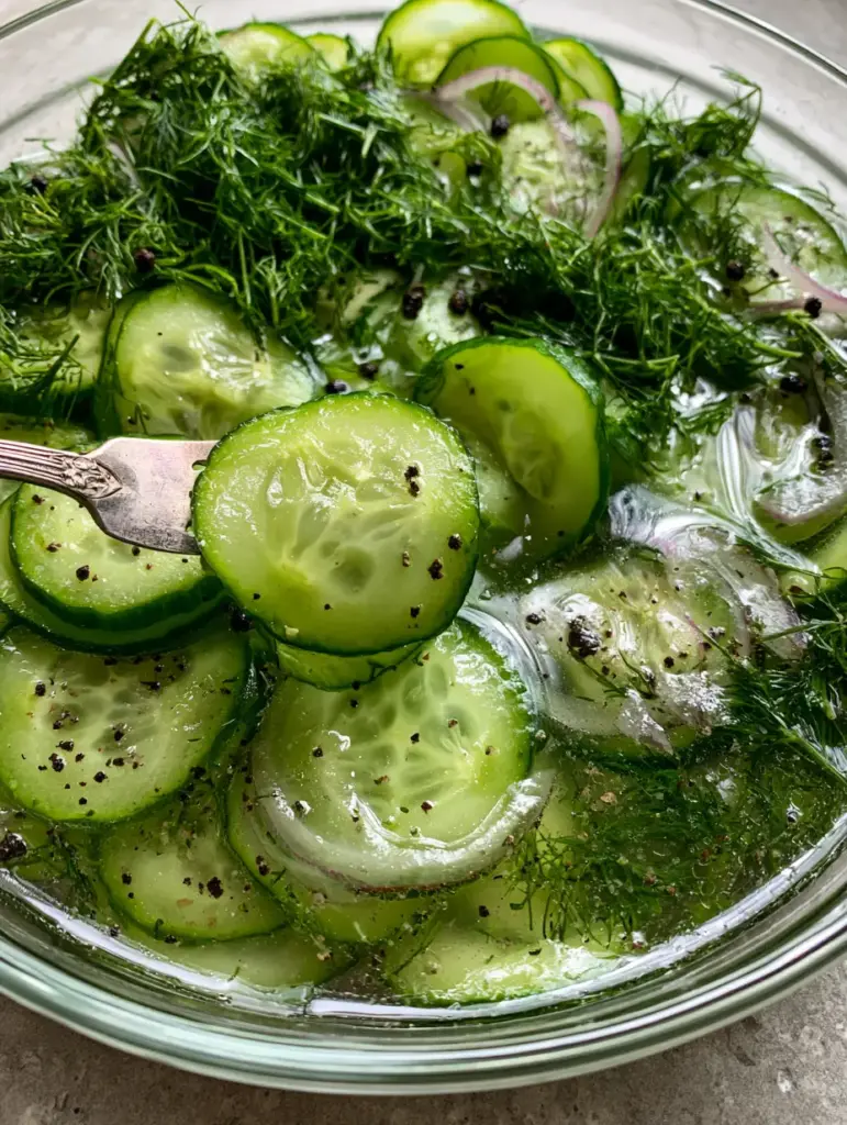 Cucumbers and Onions in Vinegar: The Ultimate Crisp Summer Salad 1 A vintage silver fork lifting a semi-translucent cucumber slice from a glass bowl of Cucumbers and onions in vinegar.