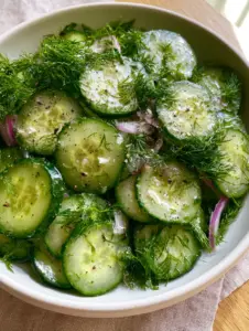 A close-up of translucent cucumber rounds tossed with feathery dill and violet red onions for a dill cucumber salad.
