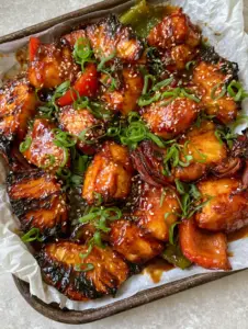 A smartphone photo of succulent chunks of seared chicken breast drenched in a thick amber glaze with charred pineapple on white parchment paper. (Gluten-free Hawaiian Chicken)