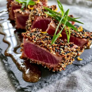 Close up of thick-cut pan-seared tuna steaks sliced into 1-inch strips with a bright ruby-red rare center and toasted sesame seeds. (pan-seared tuna steaks)